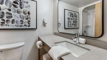 A modern bathroom with a toilet, sink, and mirror. There are framed pictures on the wall and a towel rack.