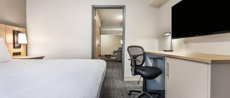 Ein Hotelzimmer mit Bett, Schreibtisch, Stuhl, Fernseher und einer Tür zu einem weiteren Raum.