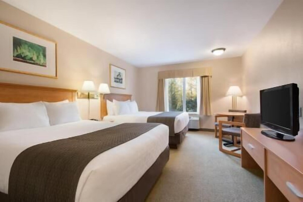 Une chambre d’hôtel avec deux lits, une télévision, un bureau et une fenêtre avec des rideaux.