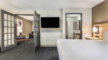 A hotel room with a bed, a TV mounted on the wall, a desk, a chair, and a bathroom visible through an open door.