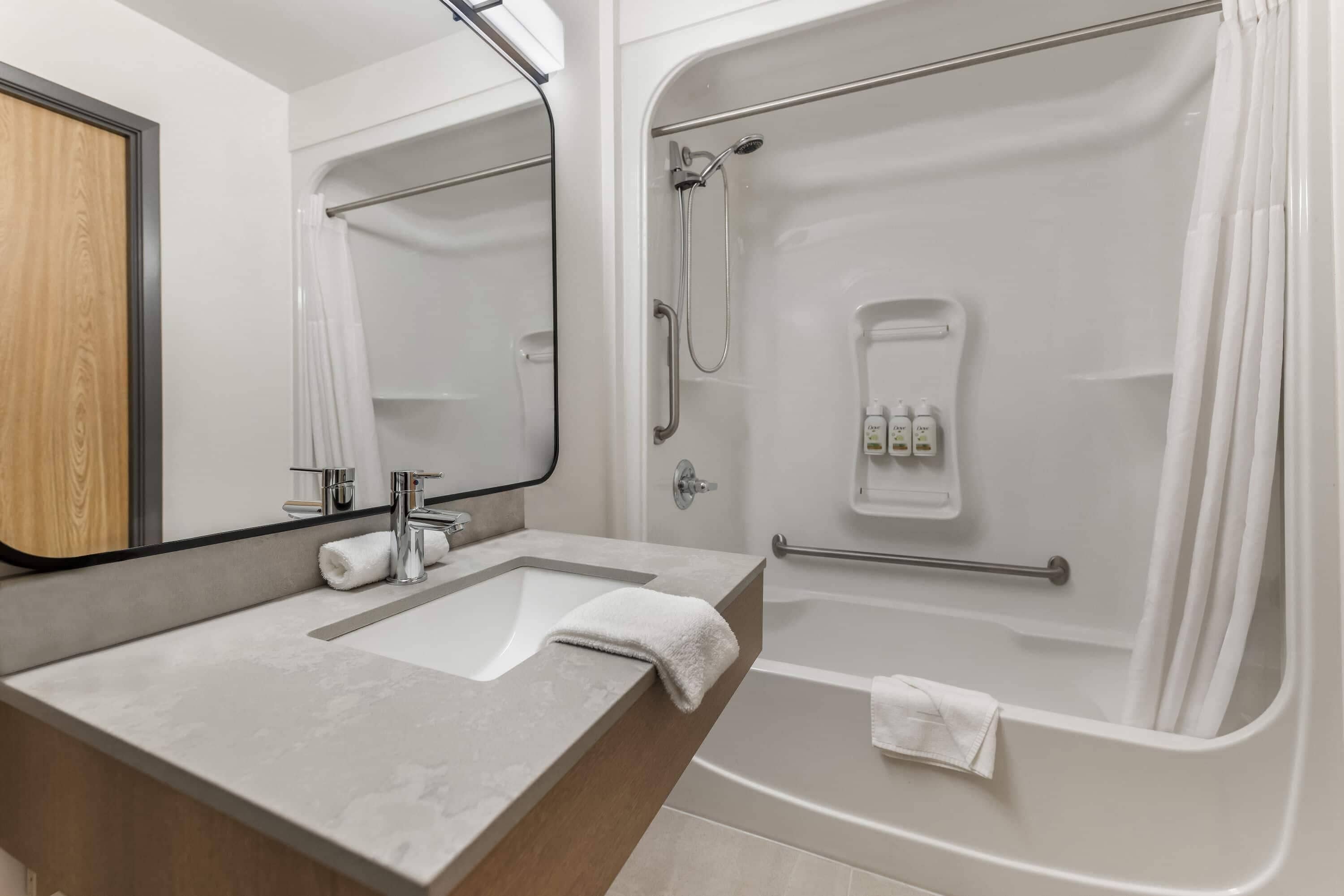 A modern bathroom with a large mirror, a sink, a shower, and a toilet.