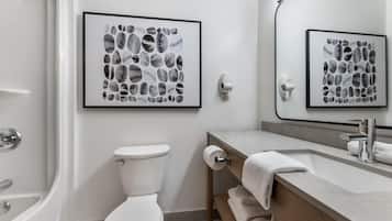 Un baño moderno con inodoro, lavamanos y ducha. Hay obras de arte enmarcadas en la pared y un perchero con toallas.