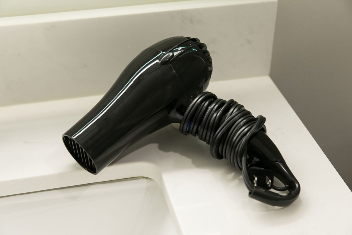 A black hair dryer with a coiled cord on a white surface.