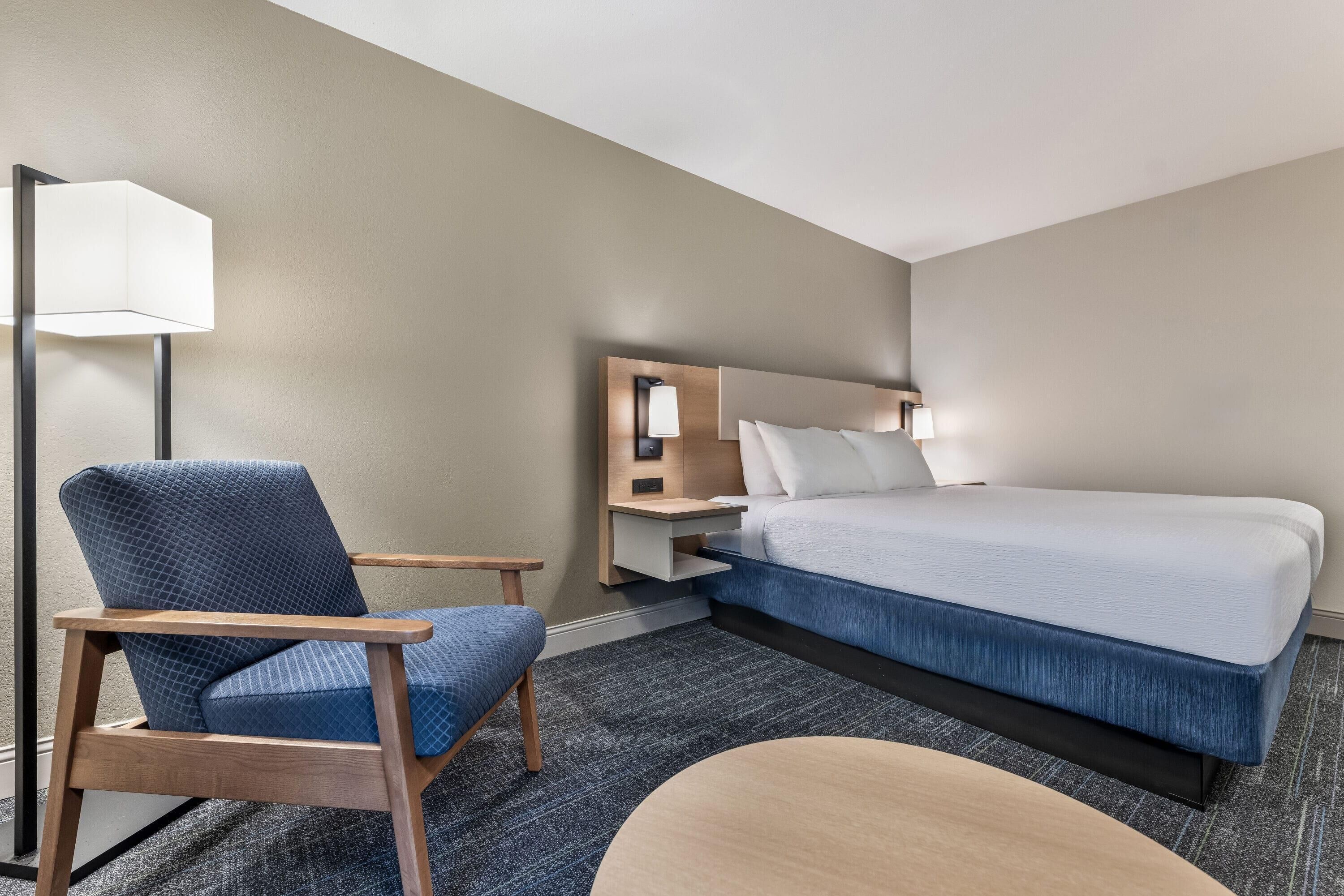 Hotellihuone, jossa on sänky, tuoli, työpöytä ja lamppu.