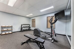 Une salle de sport équipée d’un banc, d’haltères et d’un tapis de course.