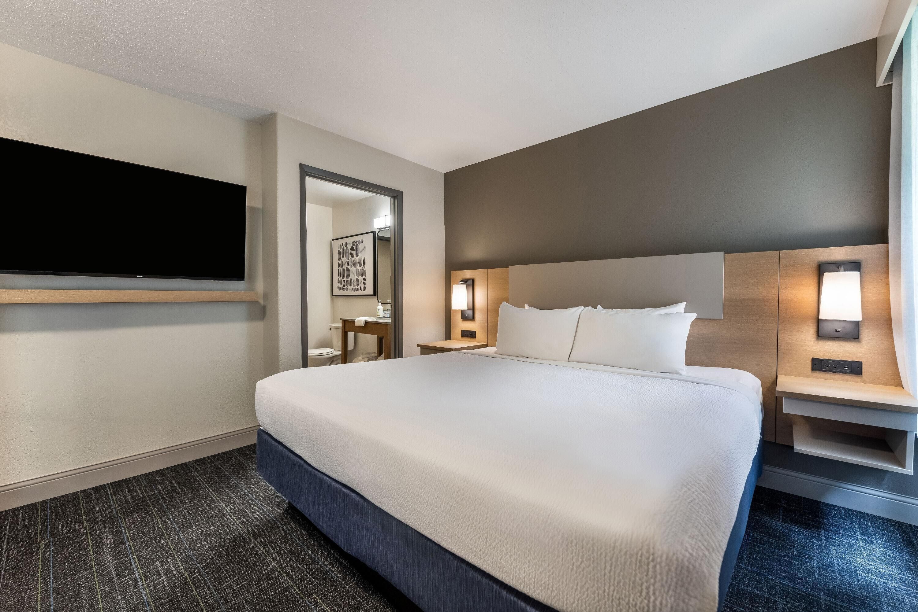 A hotel room with a large bed, bedside tables, a flat-screen TV, and a framed artwork on the wall.