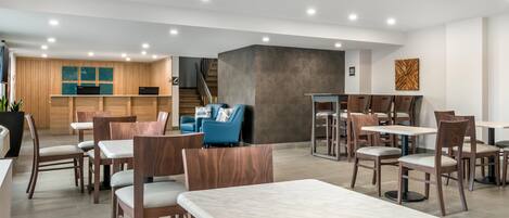 Un restaurante moderno con mesas y sillas de madera, un mostrador de recepción y una escalera que lleva a un nivel superior.