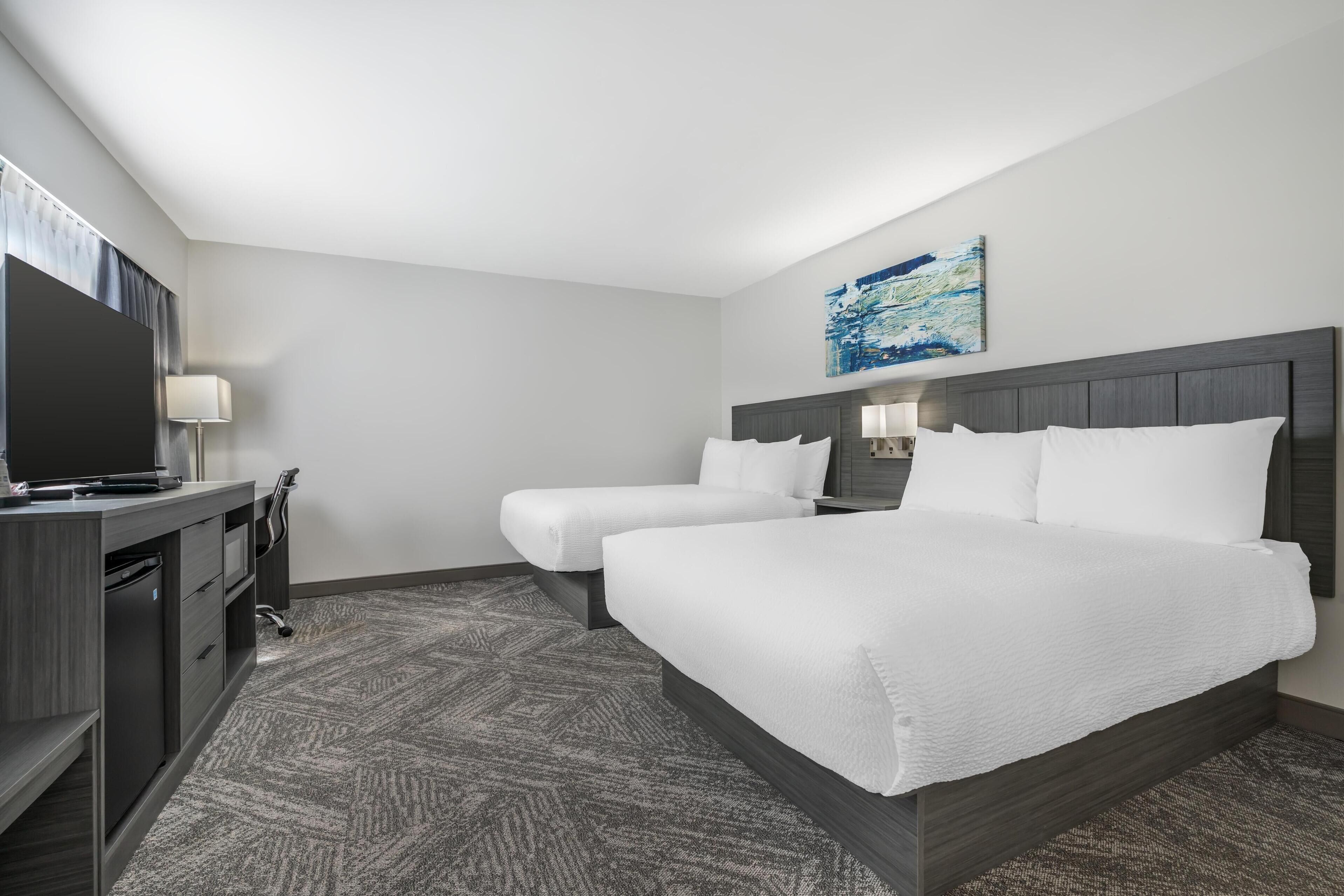 Ein Hotelzimmer mit einem großen Bett, einem Schreibtisch mit Computer und einem Fernseher.