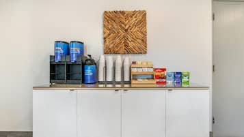 A reception area with a white cabinet, coffee dispensers, and a wall-mounted coffee machine.