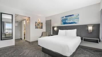A hotel room with a large bed, a desk, a chair, a wall-mounted TV, and a door leading to another room.