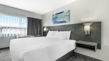 Habitación de hotel con una cama grande, cabecera con iluminación integrada, estante para televisor montado en la pared y un ventanal con cortinas.