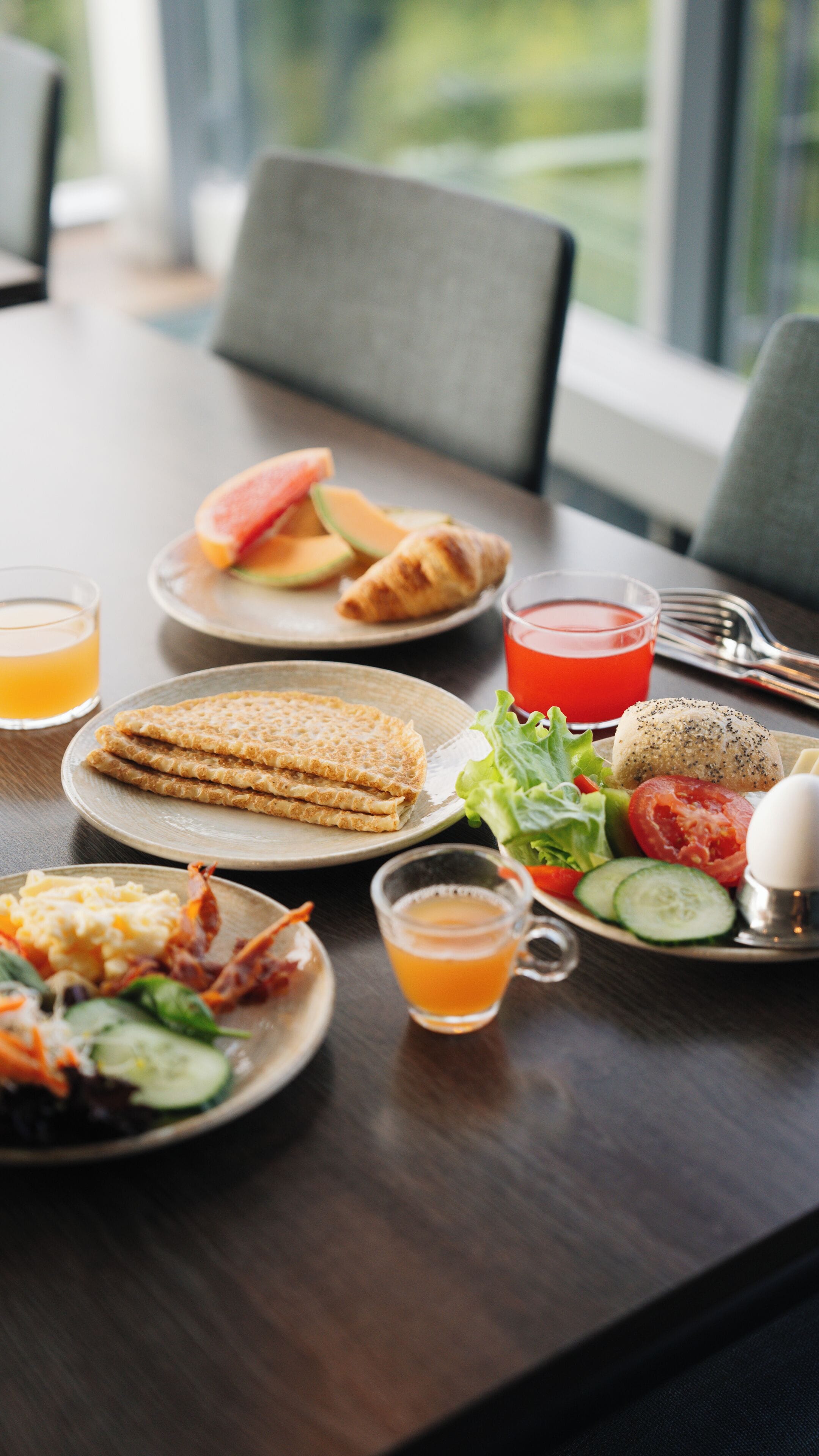 Een ontbijttafel met borden eten, waaronder croissants, een salade en een glas sinaasappelsap.