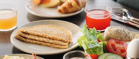 Una mesa de desayuno con platos de comida, incluyendo croissants, una ensalada y un vaso de zumo de naranja.