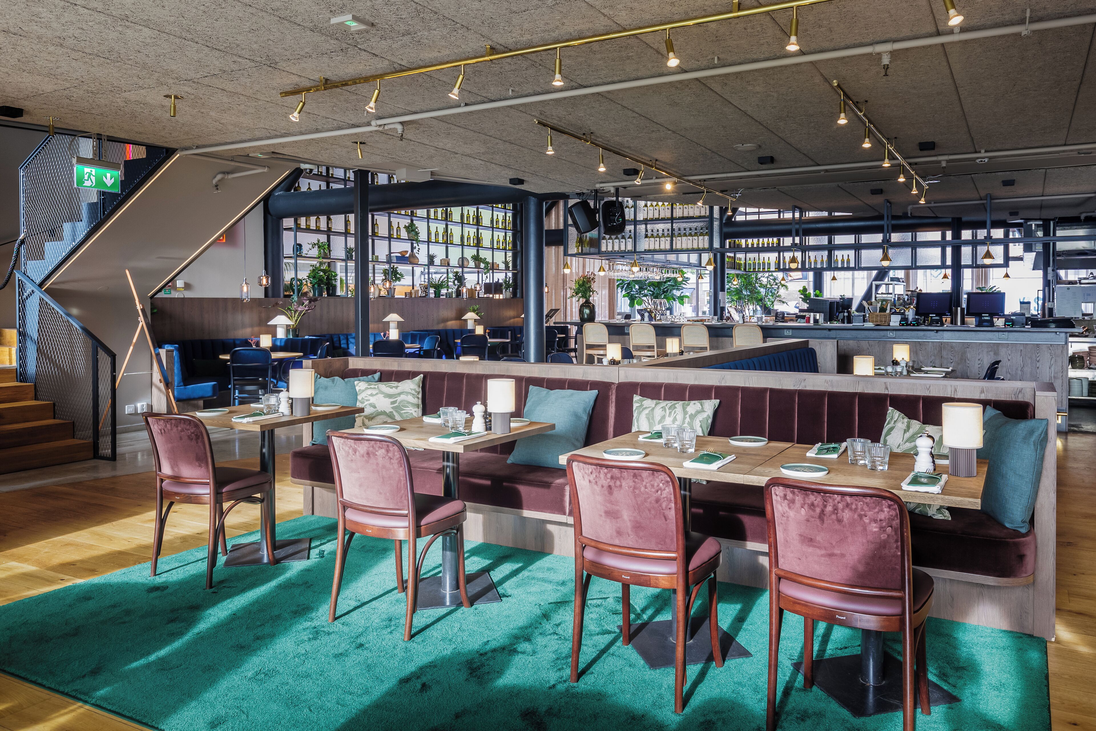 Un restaurante moderno con zona de bar, asientos con mesas y sillas, y una escalera que lleva a un nivel superior.