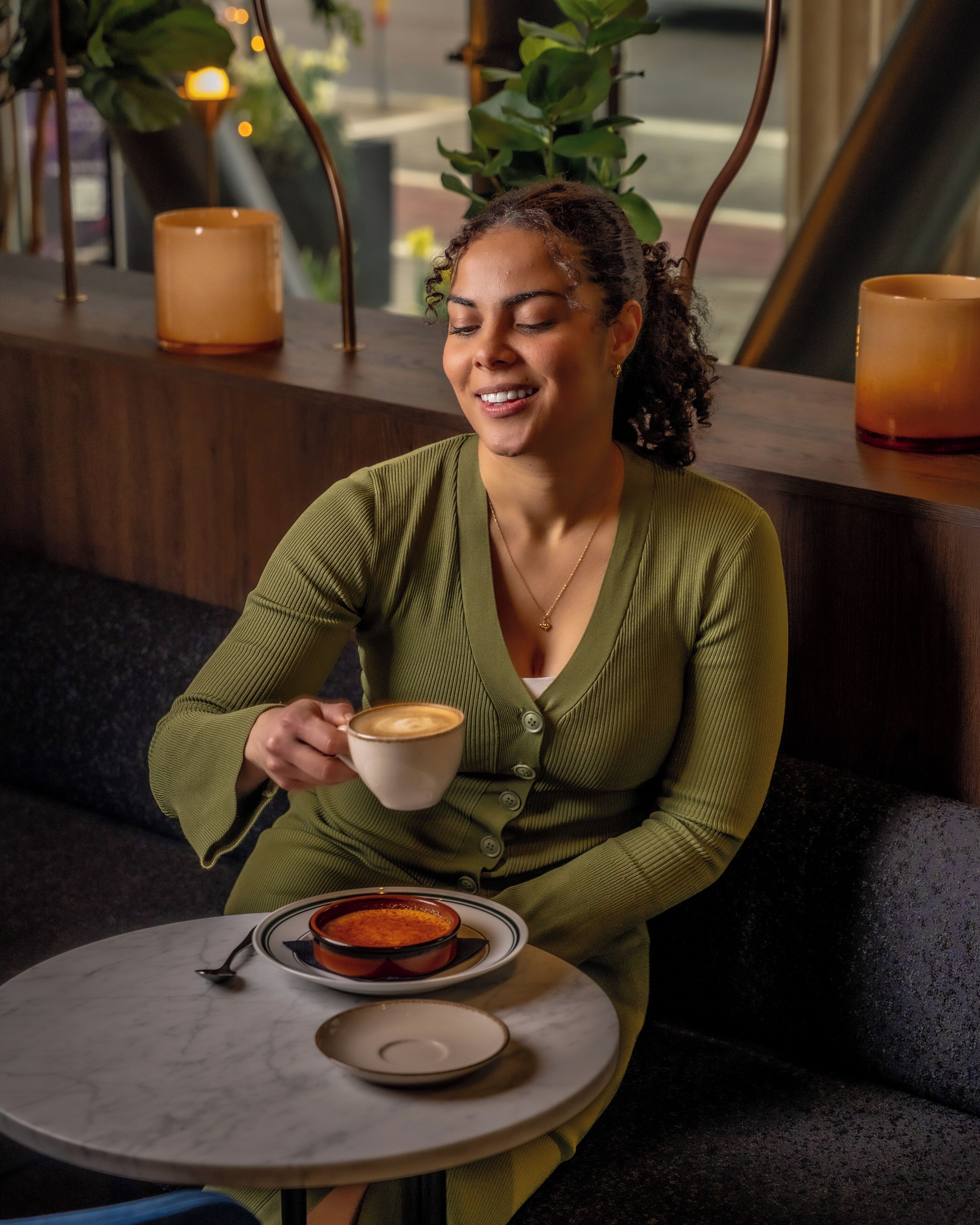 A person sitting at a round table with a cup of coffee and a dessert plate.