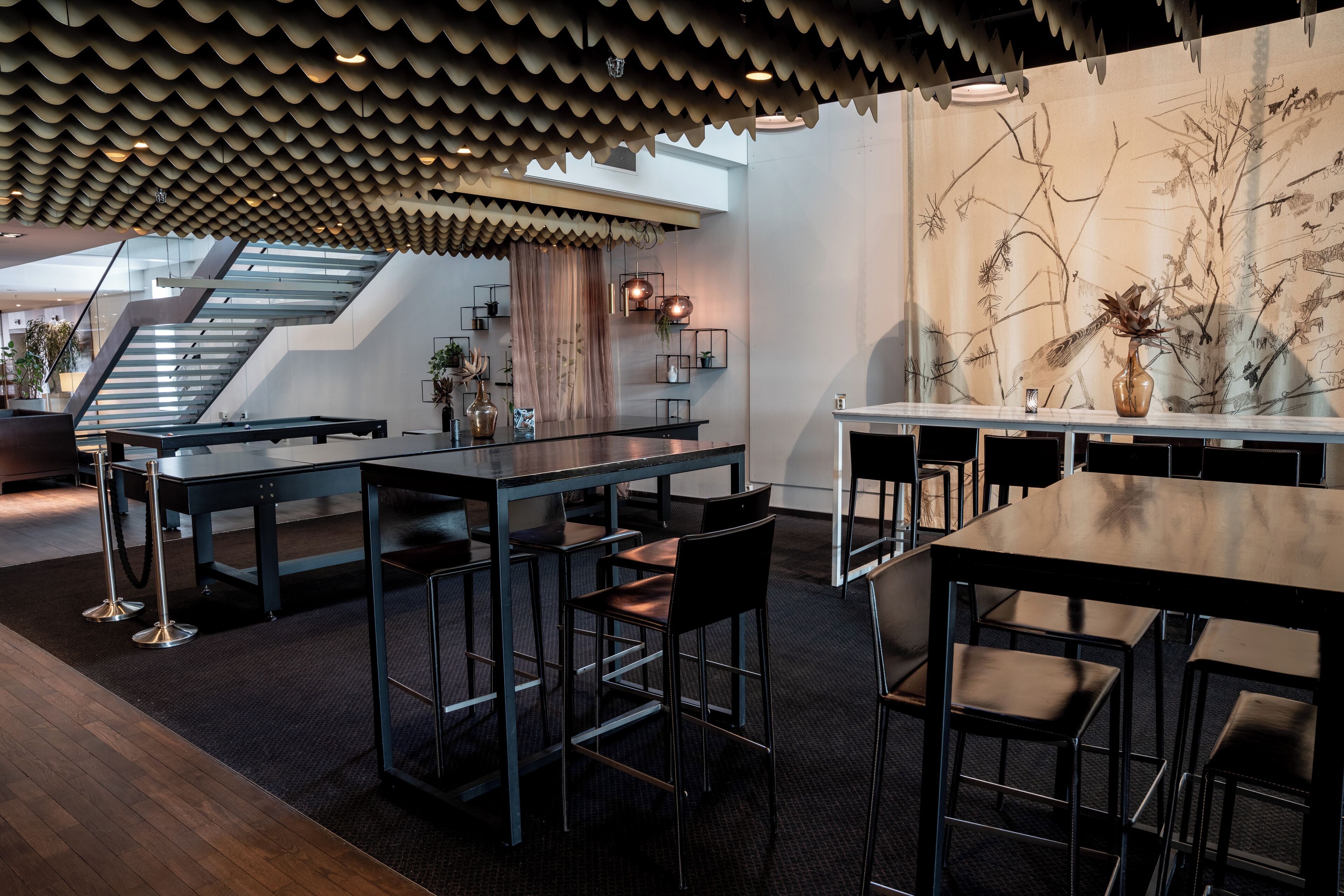 A modern interior with a dining area featuring a long table and multiple chairs, a staircase, and a wall with botanical artwork.