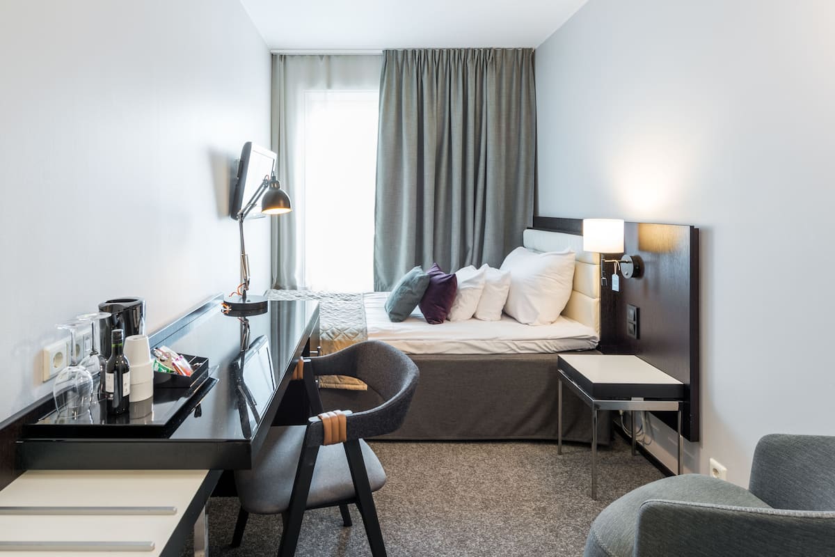 Una camera d'albergo con un letto, una scrivania, una sedia, una lampada e un comodino.