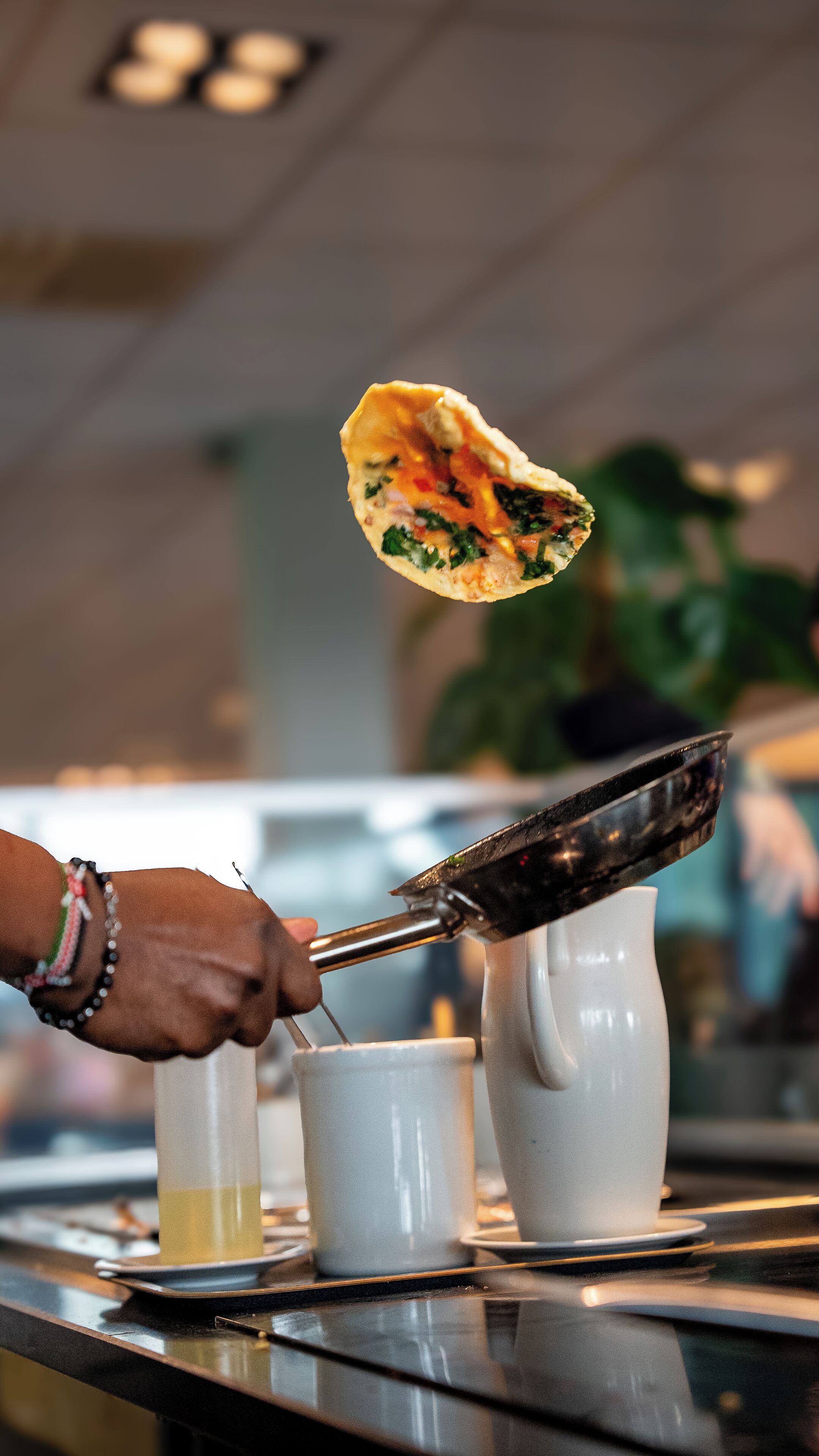 Una persona sostiene un pan plano con unas pinzas sobre una taza, probablemente en un restaurante.
