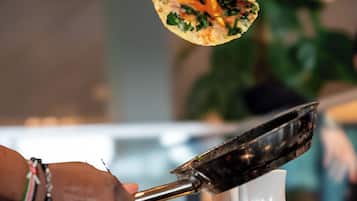 A person holding a flatbread with tongs over a cup, likely in a restaurant setting.