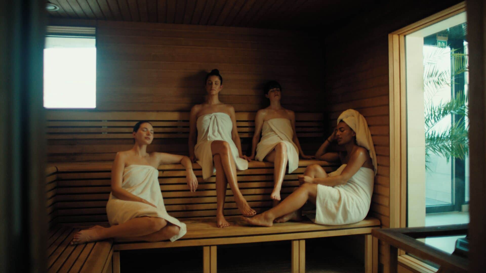 Four individuals seated on wooden benches in a room with a sloped ceiling and large windows.