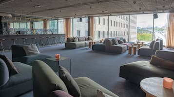 Et moderne loungeområde med sofaer og bardisk, store vinduer med udsigt over byen.