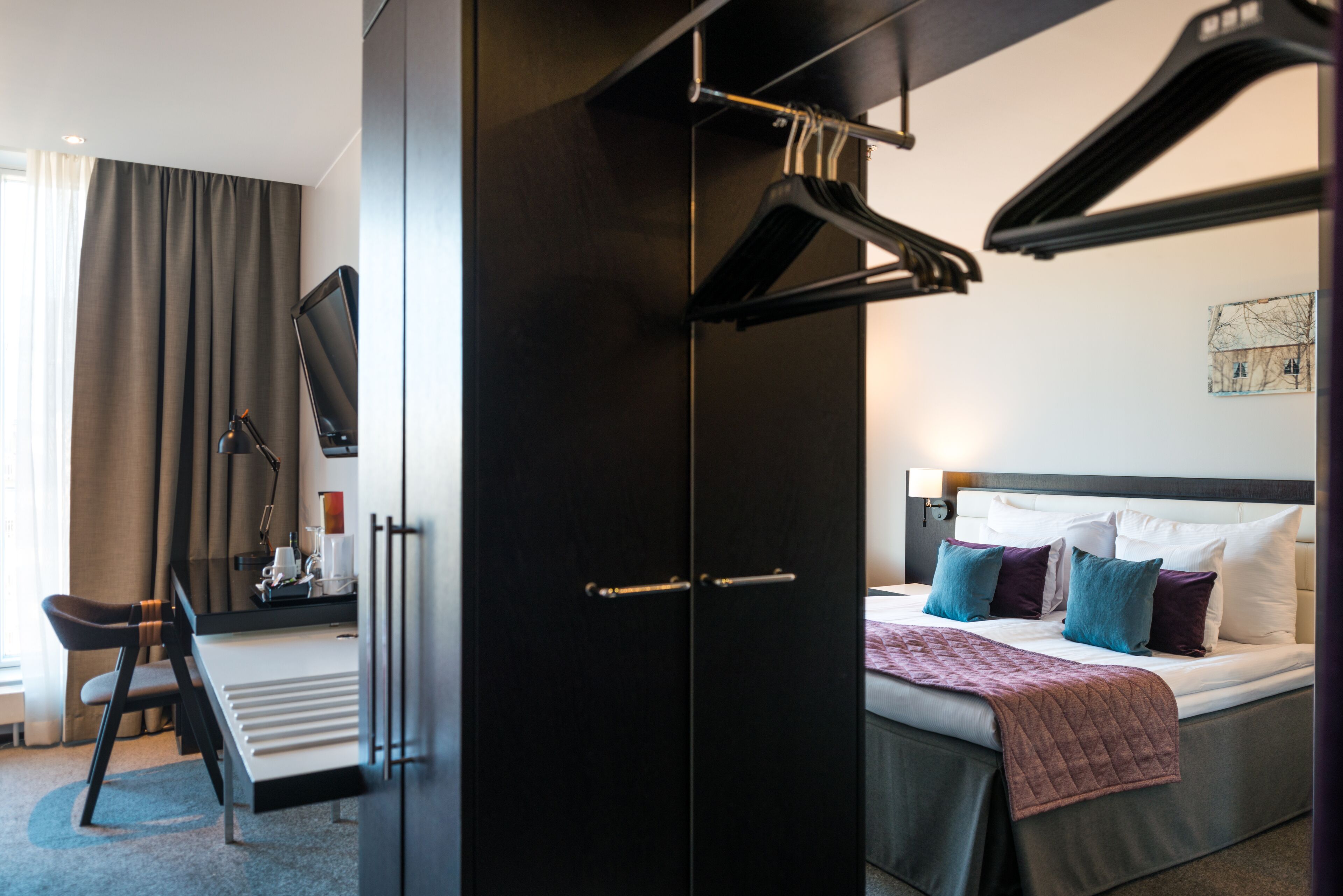Ein modernes Hotelzimmer mit Bett, Schreibtisch und Kleiderschrank.
