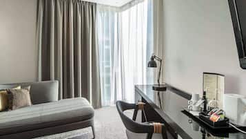 Habitación de hotel con cama, escritorio con lámpara, silla, cafetera y televisor.