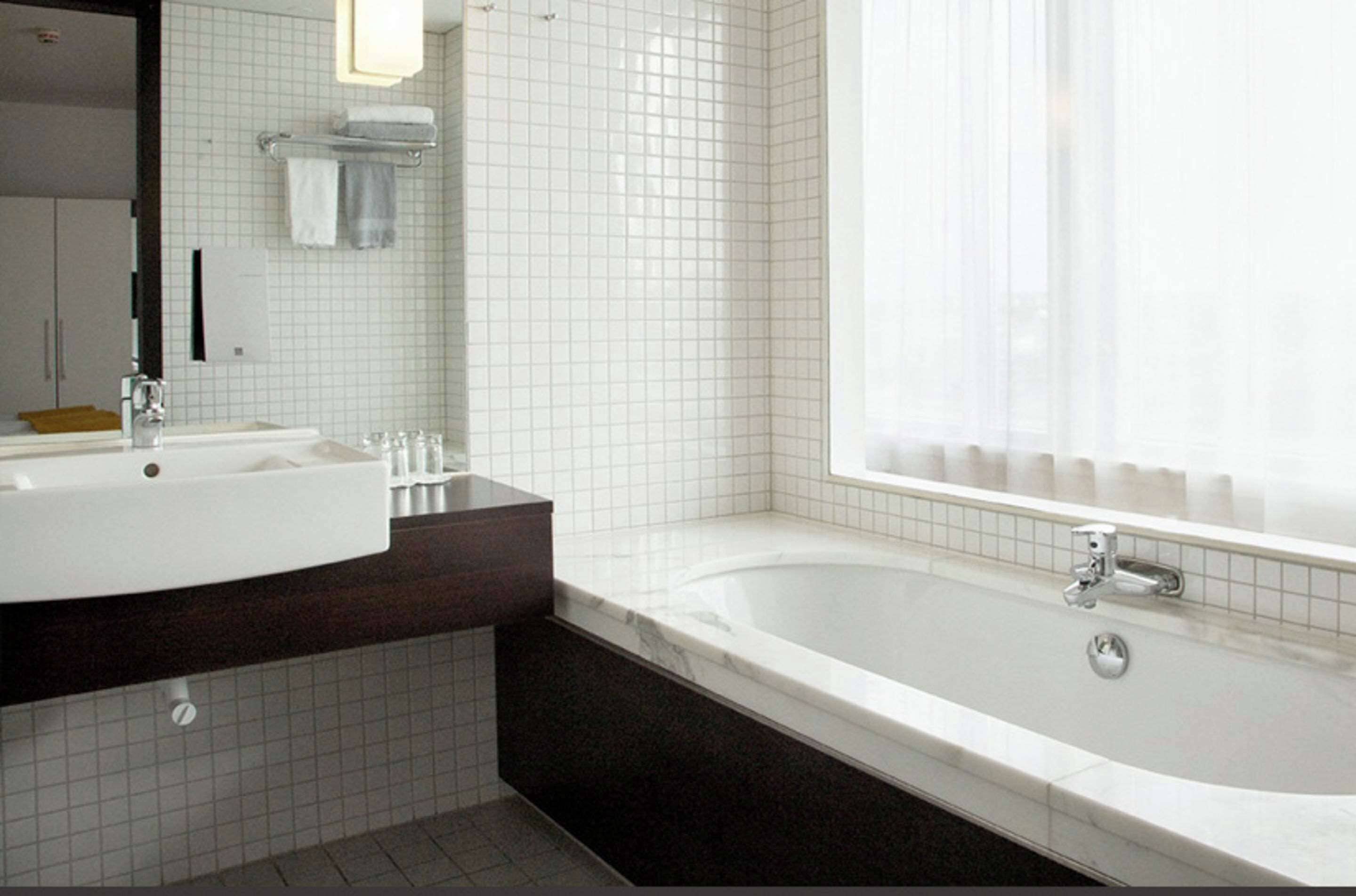 A modern bathroom with a white sink, dark countertop, and a large bathtub.