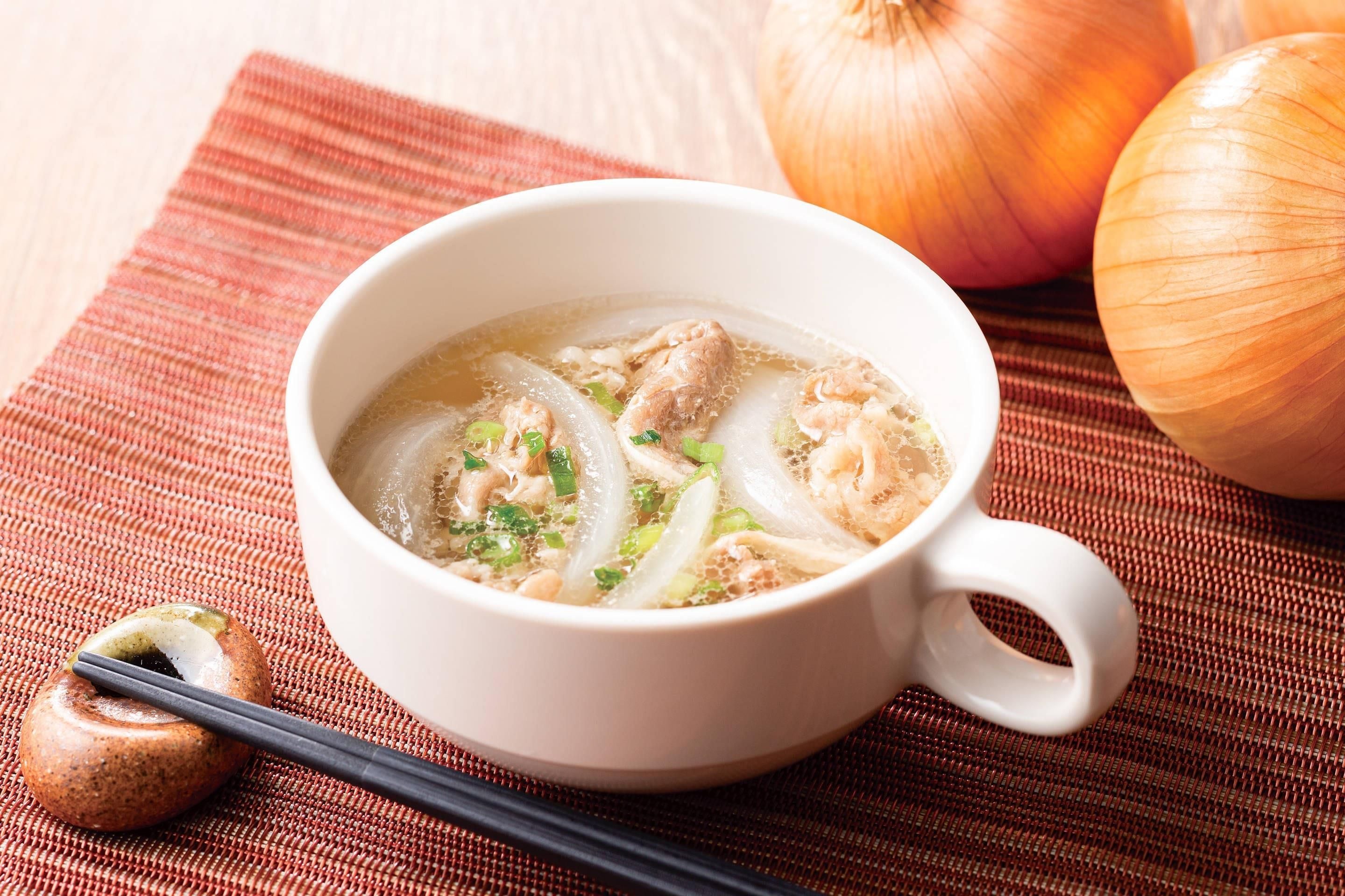 A bowl of soup with chicken and onions on a woven mat.