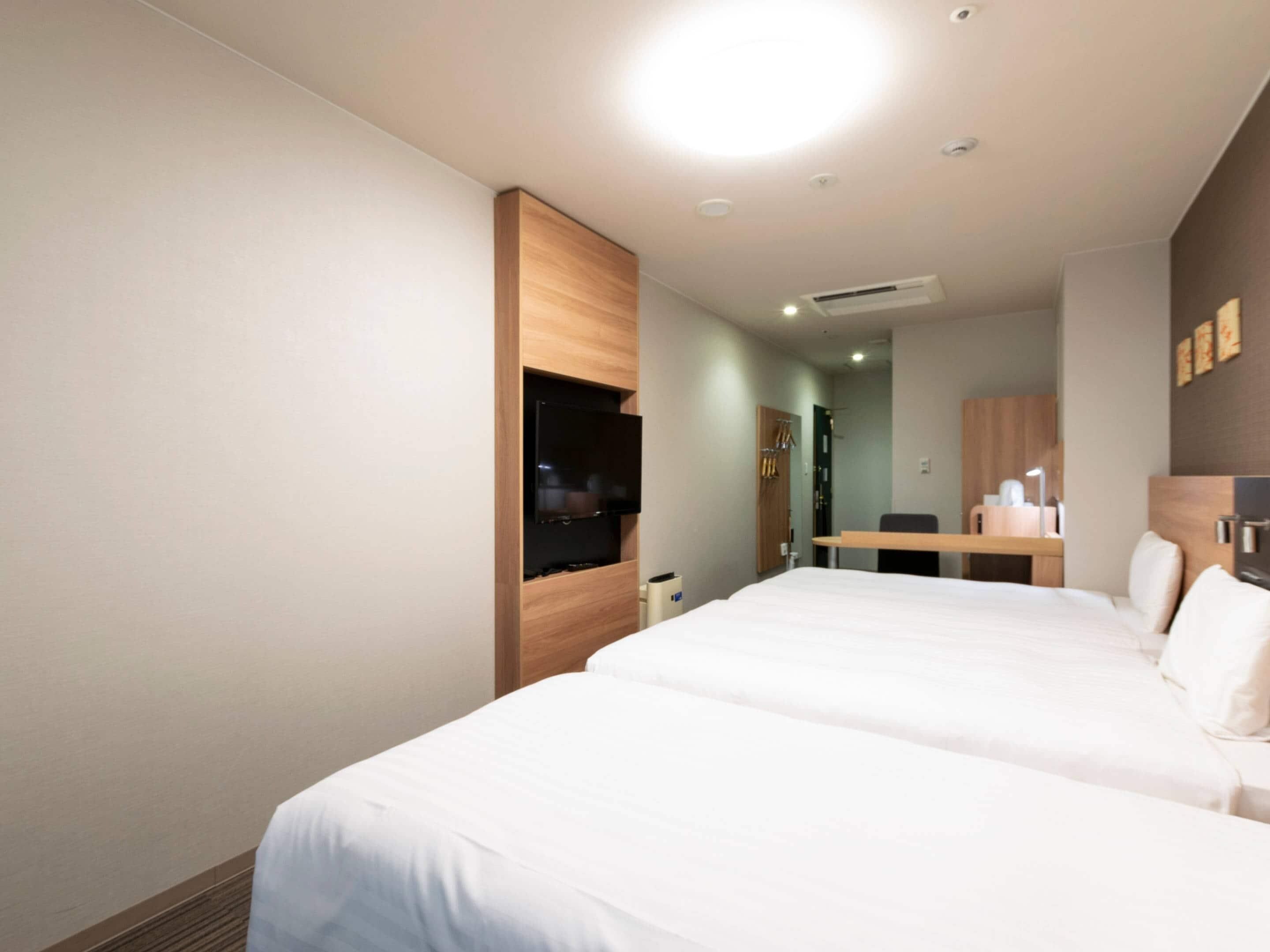 A hotel room with a large bed, a desk, a mirror, and a television.