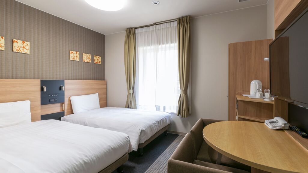 Ein Hotelzimmer mit zwei Betten, einem Schreibtisch, einem Telefon, einer Kaffeemaschine und einem Fernseher.