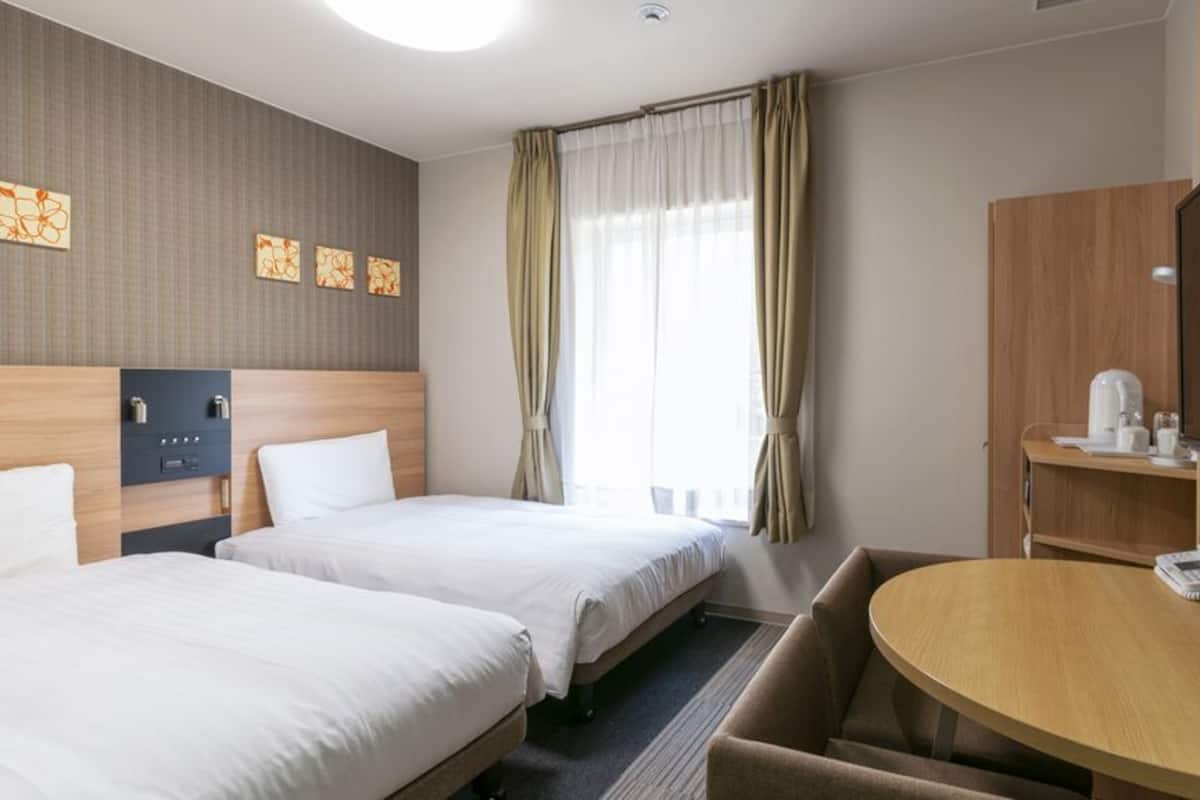 Een hotelkamer met twee bedden, een bureau met telefoon, een koffiezetapparaat en een televisie.