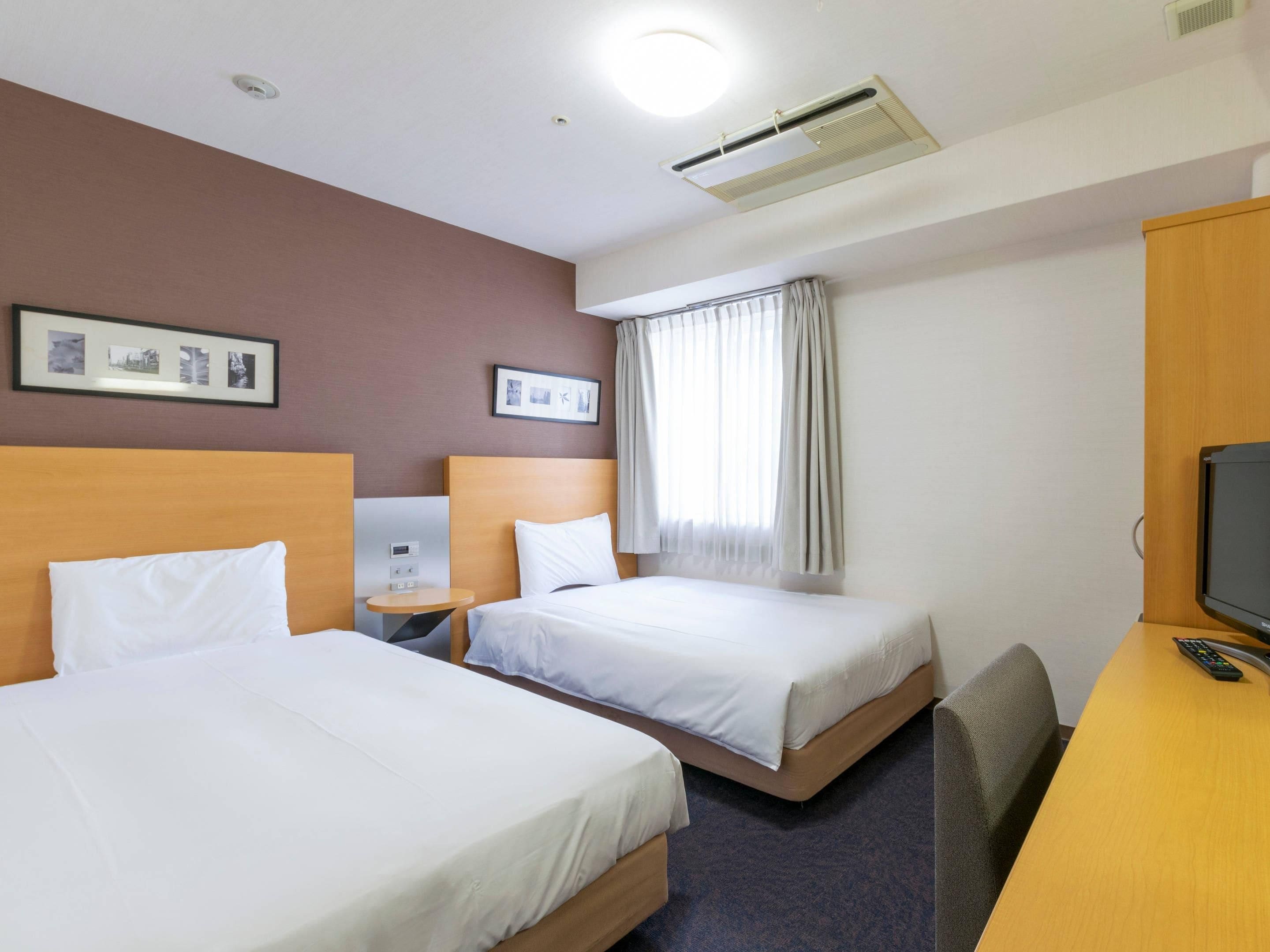 A hotel room with two beds, a desk, a TV, and a window with curtains.