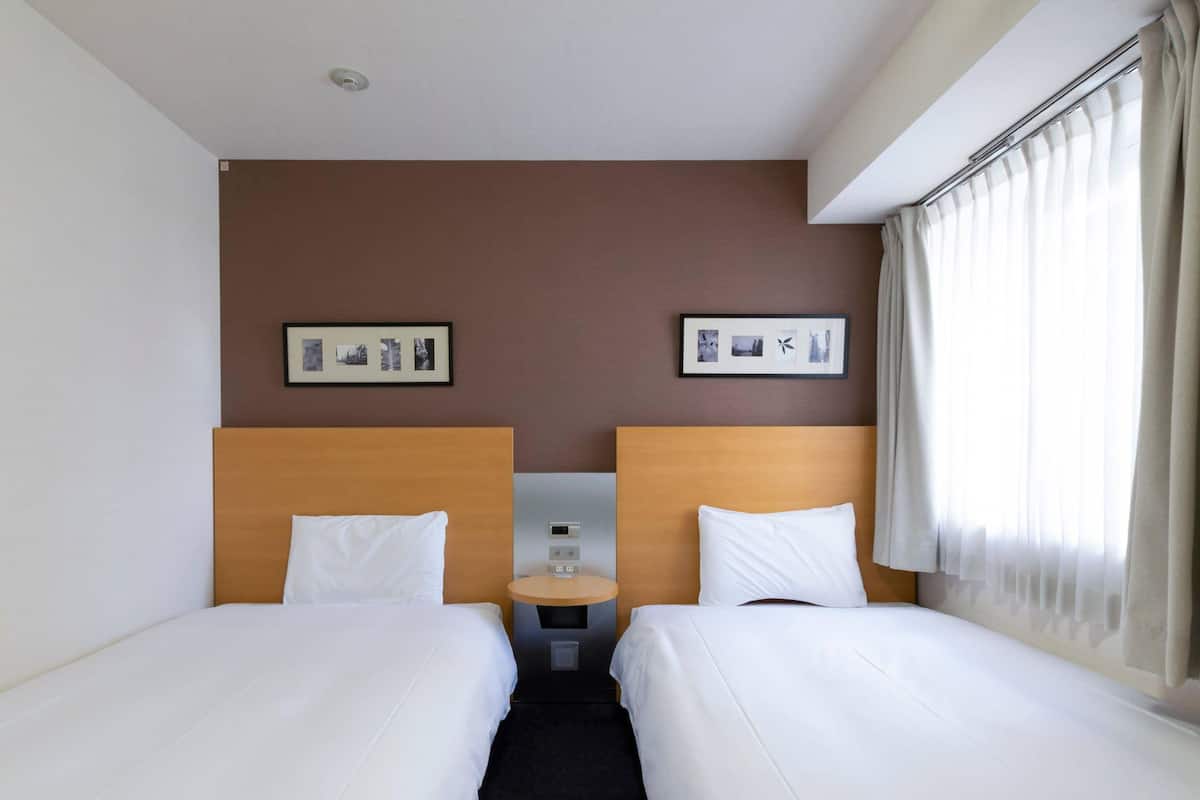 Een hotelkamer met twee eenpersoonsbedden, een nachtkastje met een digitale klok en twee ingelijste foto's aan de muur.