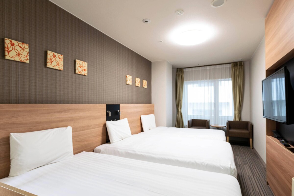 Een hotelkamer met twee bedden, een televisie, een bureau en een raam met gordijnen.