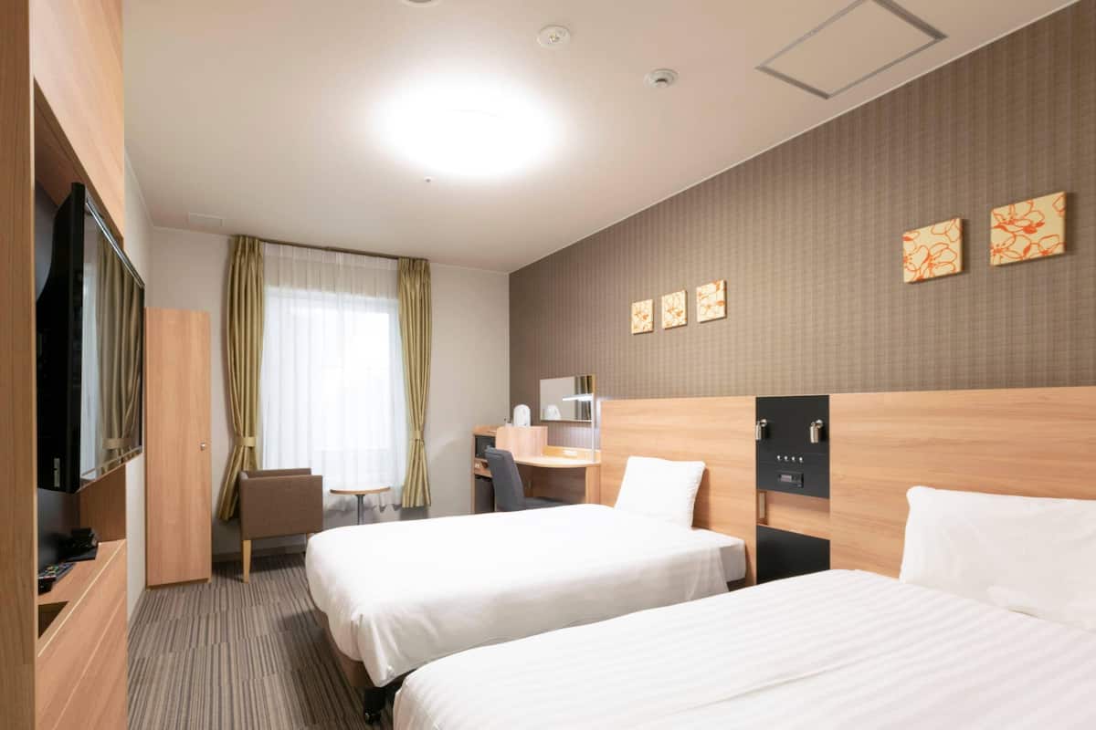 Een hotelkamer met twee bedden, een bureau, een stoel, een televisie en een raam met gordijnen.