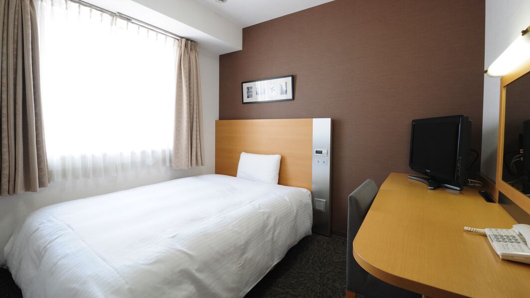 Ein Hotelzimmer mit einem Bett, einem Schreibtisch mit Computer, einem Telefon und einem Fenster mit Vorhängen.