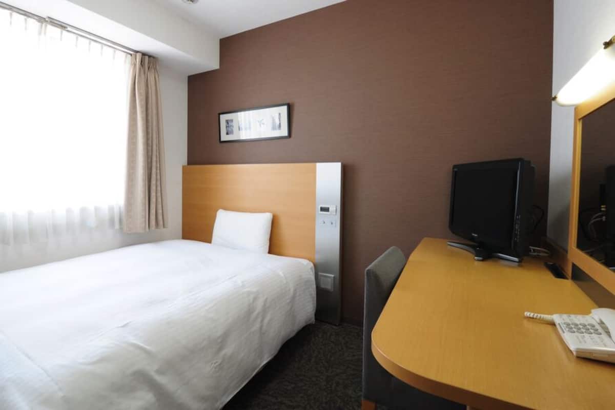 Een hotelkamer met een bed, een bureau met computer, een telefoon en een raam met gordijnen.