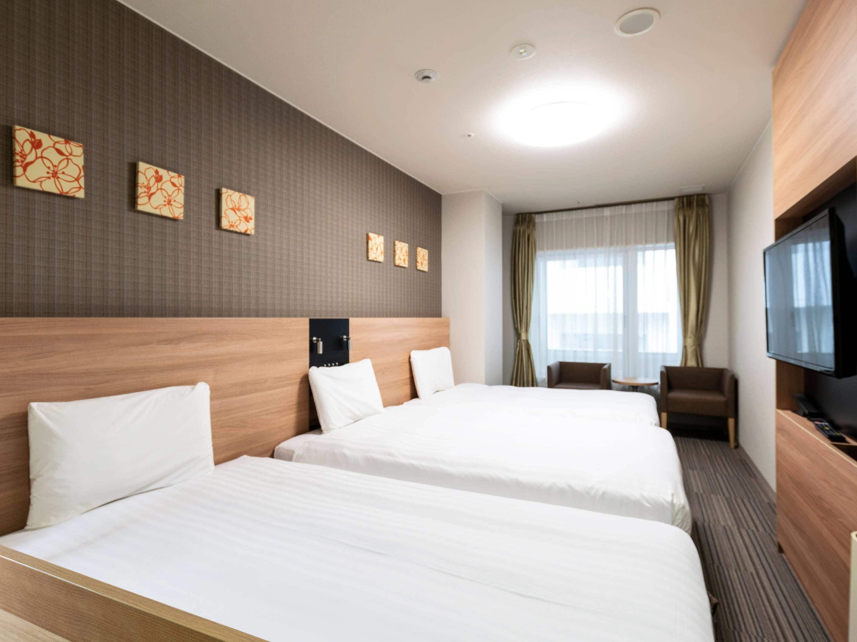 A hotel room with two beds, a TV, a desk, and a window with curtains.