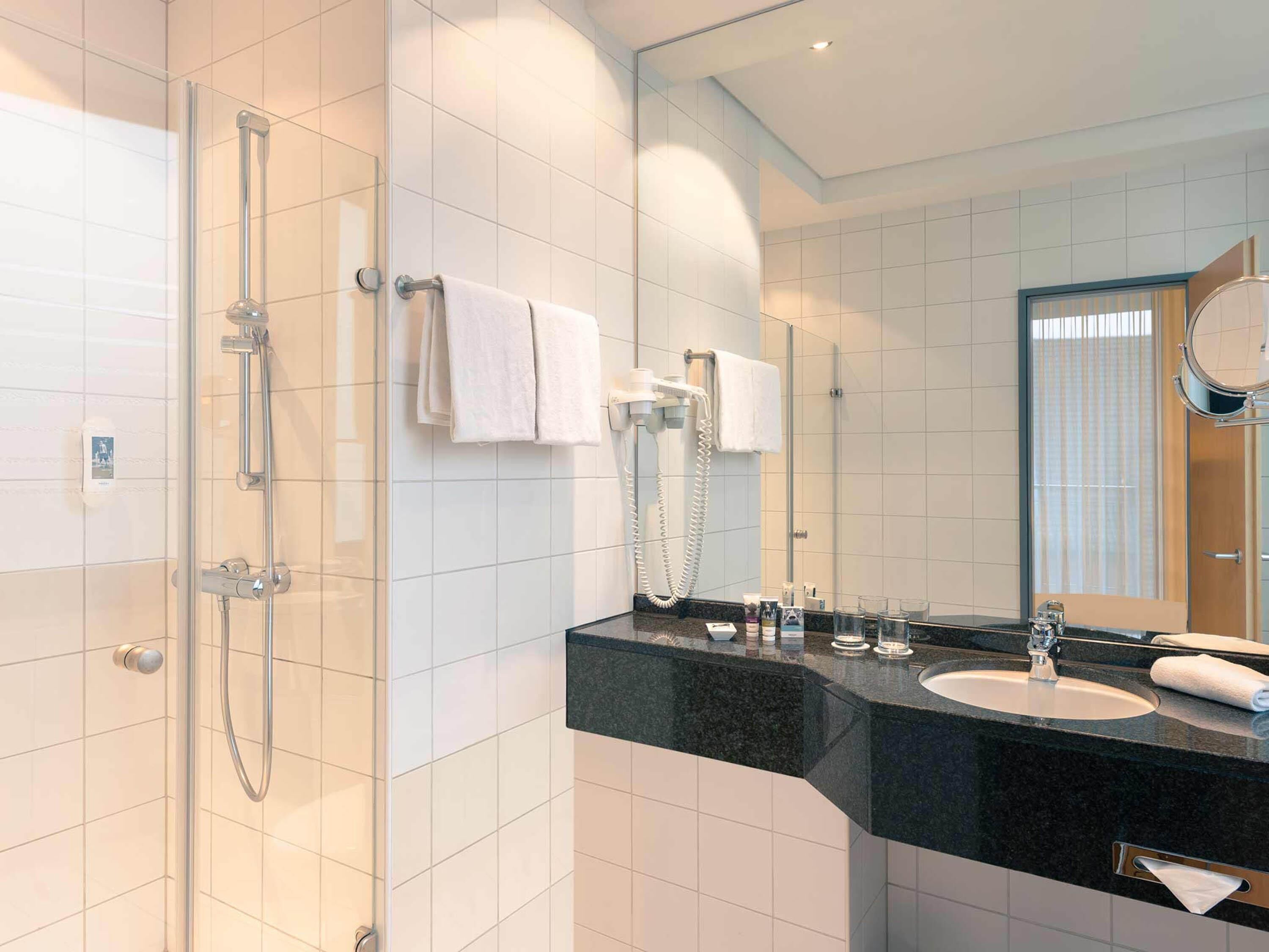 Un baño moderno con cabina de ducha de vidrio, encimera negra, lavabo y espejo.