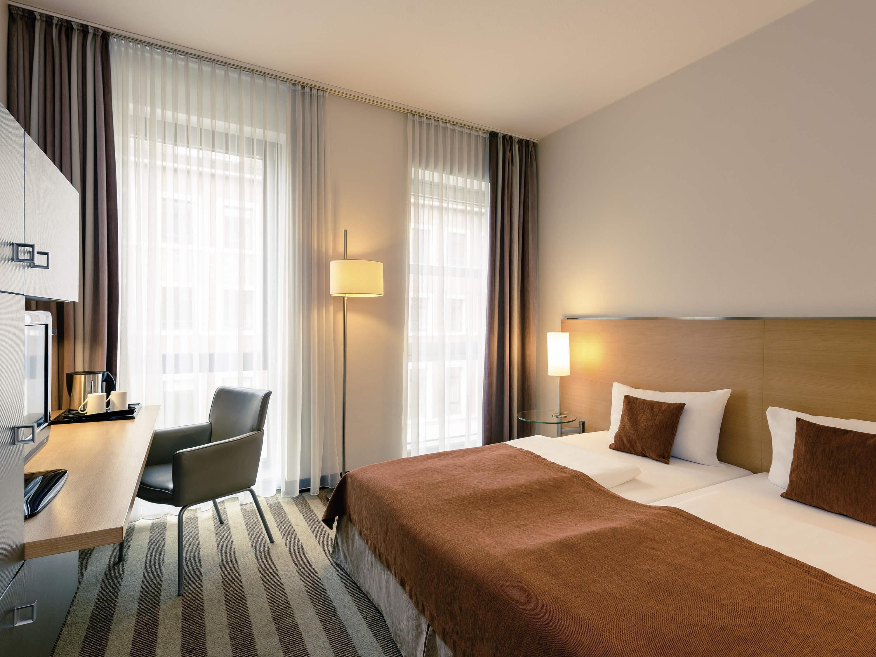 Een hotelkamer met een bed, een bureau met stoel, een lamp en een televisie.
