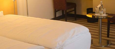 Habitación de hotel con cama, escritorio, silla, televisor y una mesita con una botella.