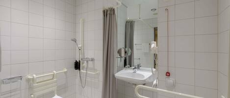 A modern bathroom with white tiles, a shower with a handheld showerhead, a sink with a mirror, and a toilet.