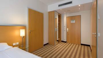 A hotel room with a bed, a nightstand, a lamp, a mirror, and a door leading to a bathroom.