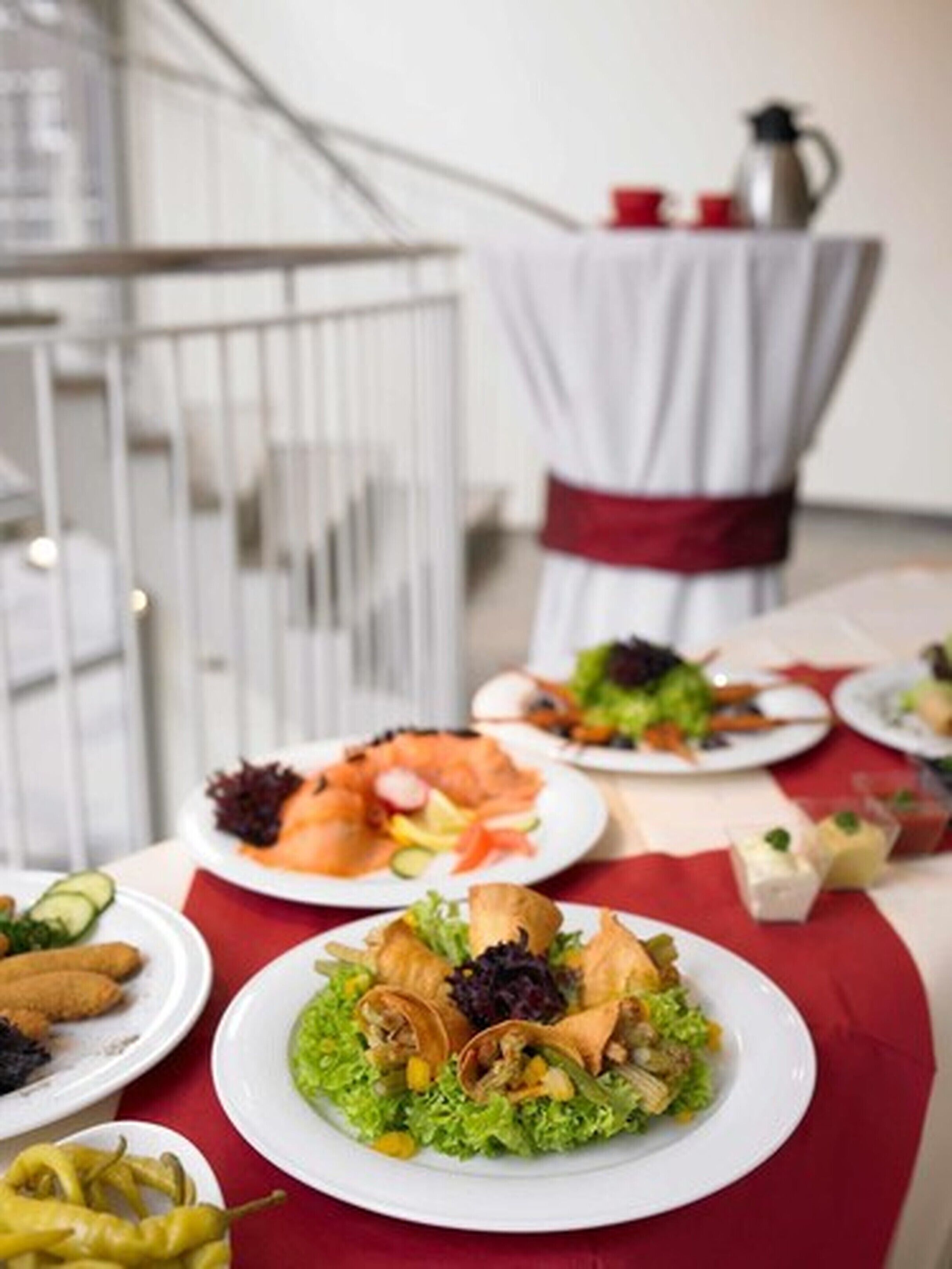 Una mesa de comedor con varios platos, incluyendo ensaladas y mariscos, en un ambiente moderno con una escalera y una cafetera al fondo.