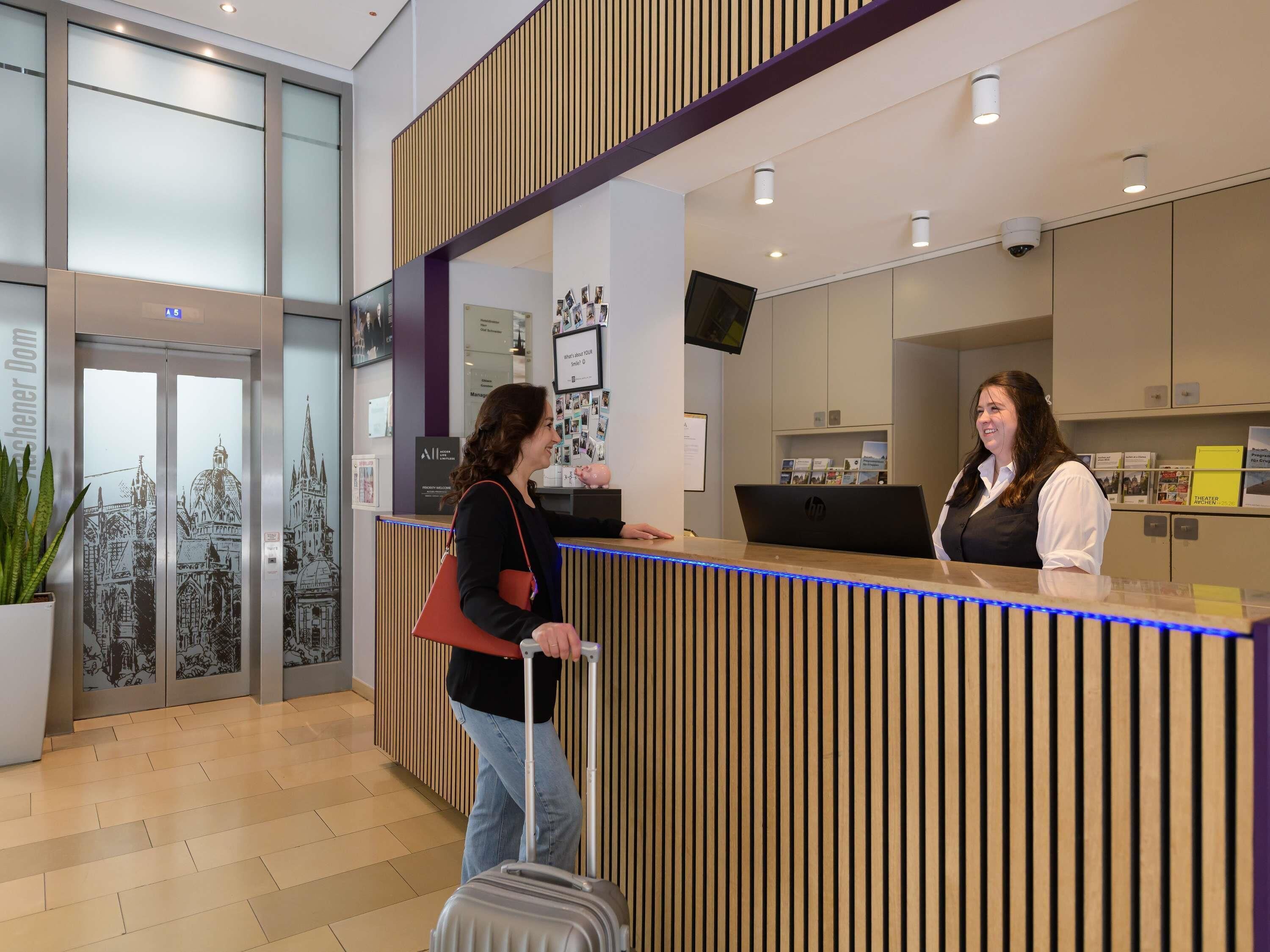 A hotel reception desk with a modern design, featuring a wooden panel backdrop, a digital screen, and a reception counter.