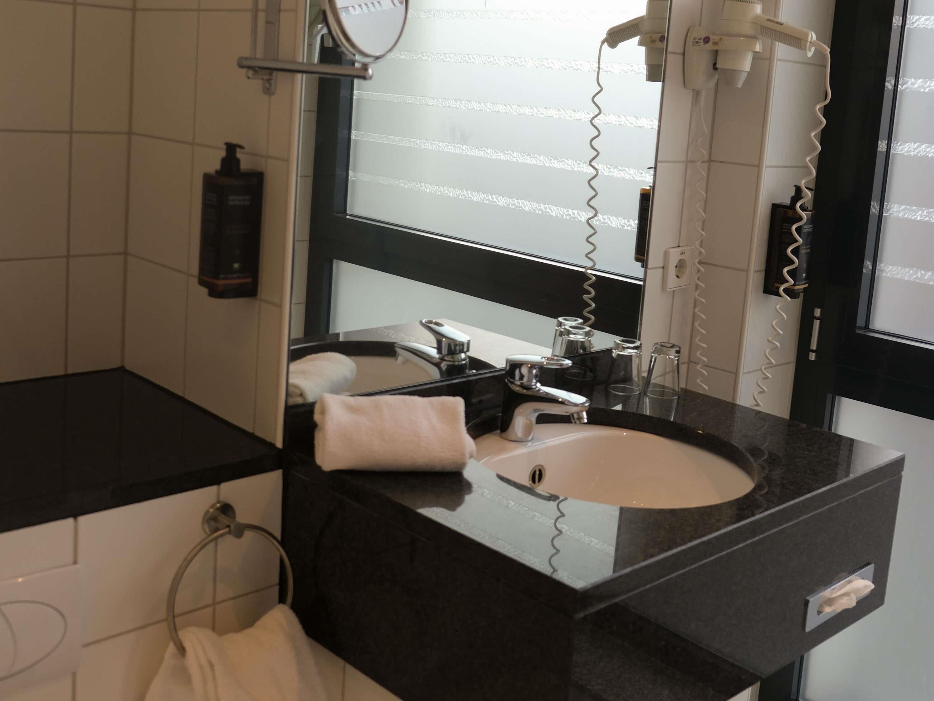 Une salle de bain moderne avec un plan de toilette noir, un lavabo blanc, un miroir et un sèche-cheveux.