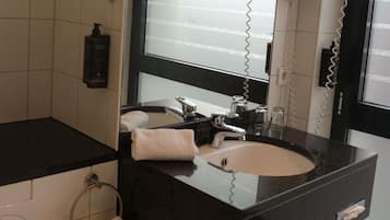 Un baño moderno con encimera negra, lavamanos blanco, espejo y secador de pelo.
