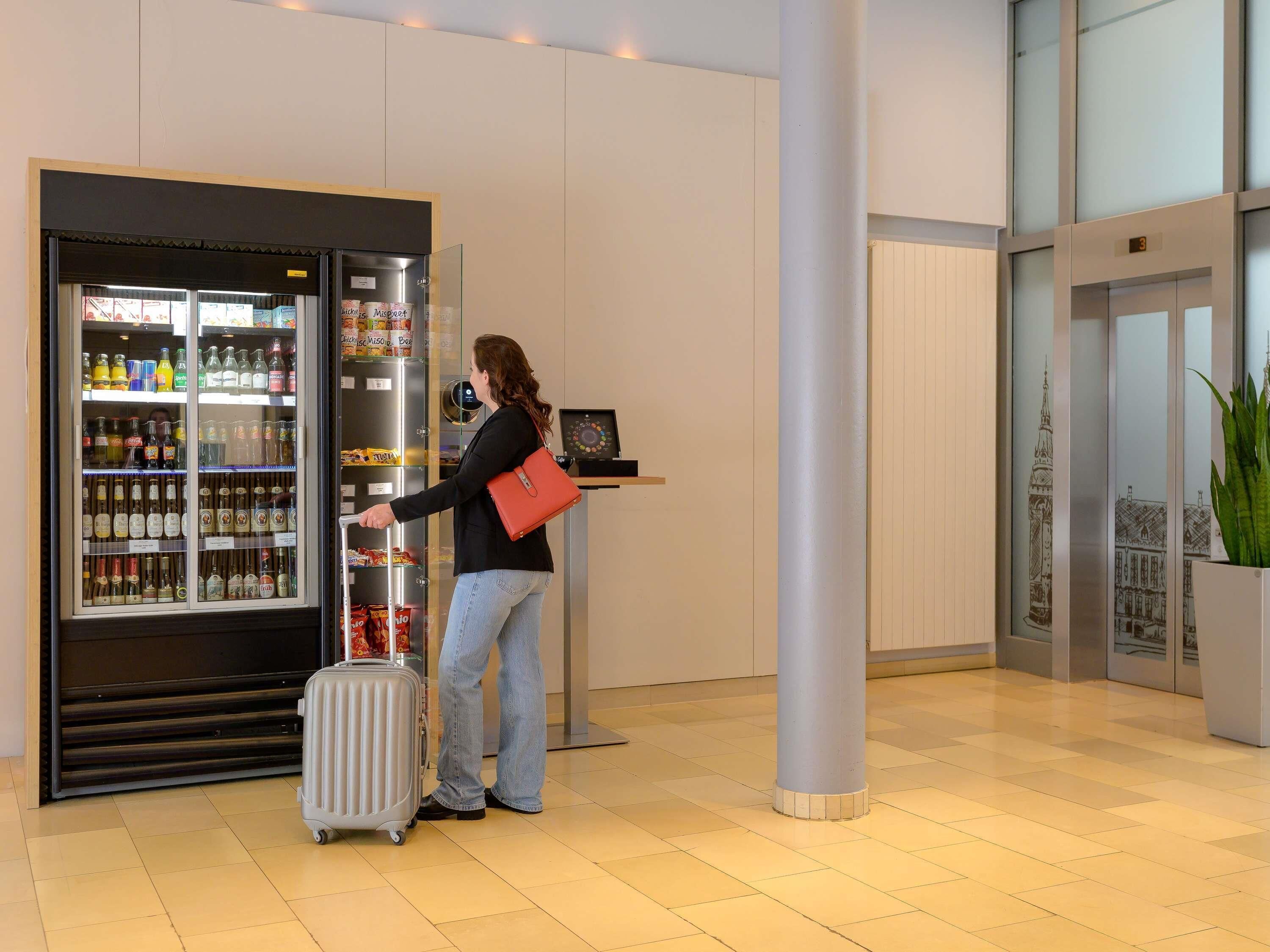 Eine Frau mit einem Koffer an einem Selbstbedienungsgetränkeautomaten in der Hotelhalle.