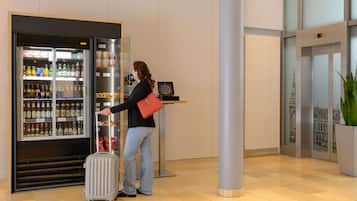 Eine Frau mit einem Koffer an einem Selbstbedienungsgetränkeautomaten in der Hotelhalle.